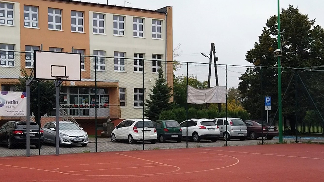 Zdjęcie przedstawia parking przed głównym wejściem do szkoły.
